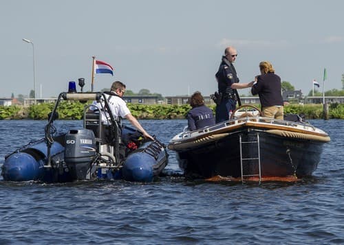 Twee agenten van de waterpolitie liggen met een rubberboot langszij een open motorboot en controleren de schipper.
